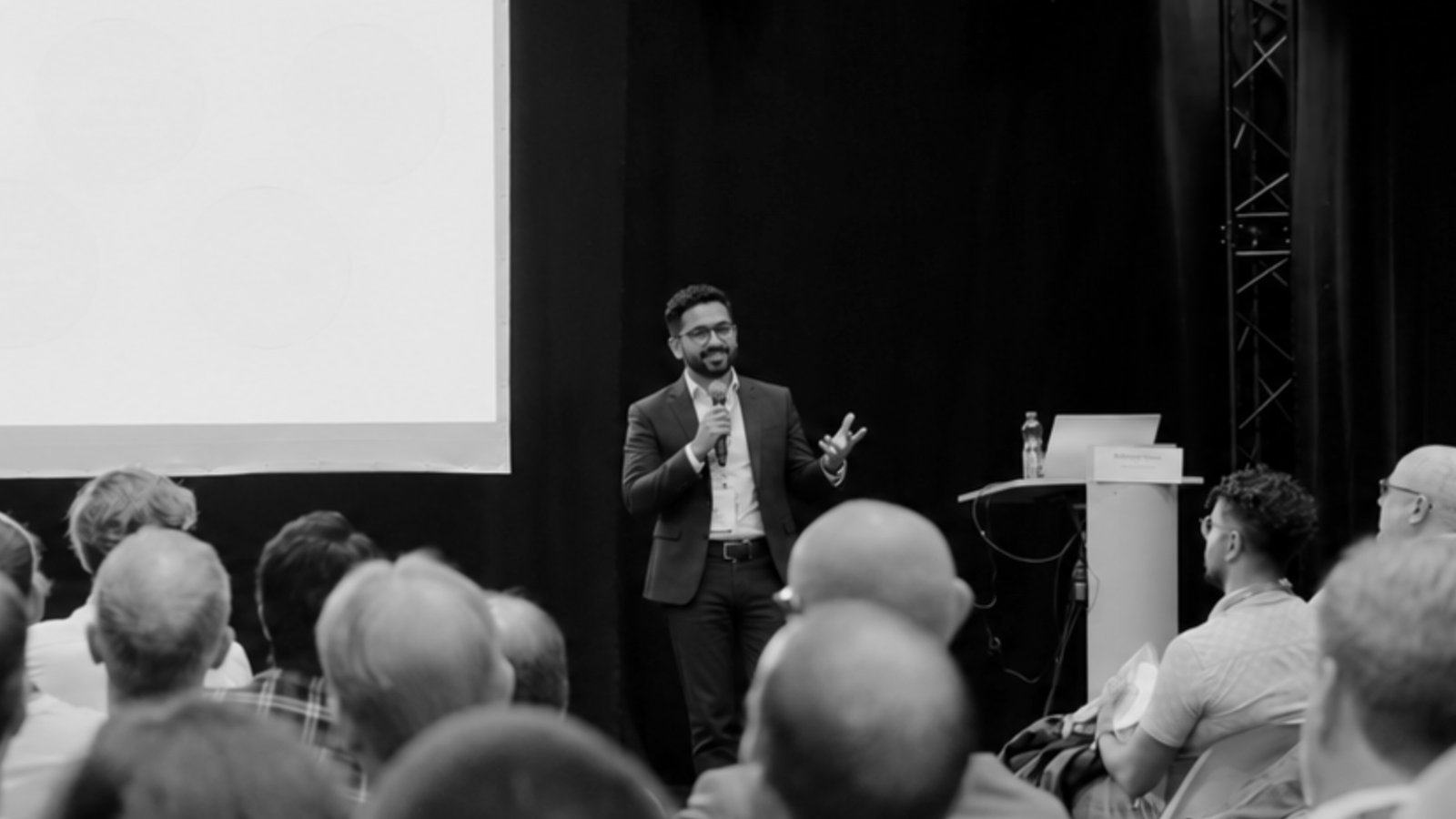 Ethan Blatti, COO of Hans Blatti, speaking on stage with a microphone in front of a full audience at a startup expo