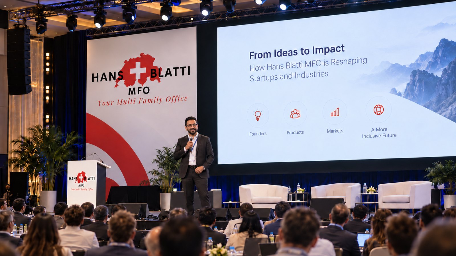 Speaker on stage in Madrid in front of the Hans Blatti MFO banner and a screen reading “From Ideas to Impact: How Hans Blatti MFO is Reshaping Startups and Industries”